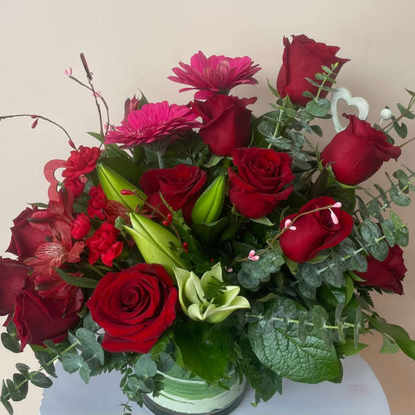 Red rose arrangement with pink gerbera daisies and mixed red blooms in a clear glass vase