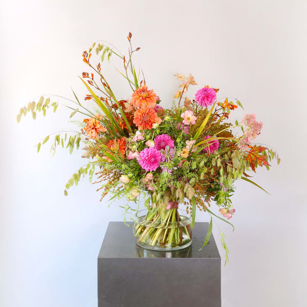 Bouquet of orange and pink dahlias with mixed wildflowers and grasses in a clear glass vase.
