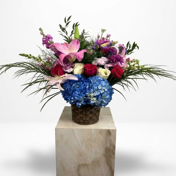 Mixed bouquet with pink lilies, roses, and blue hydrangea in a woven basket