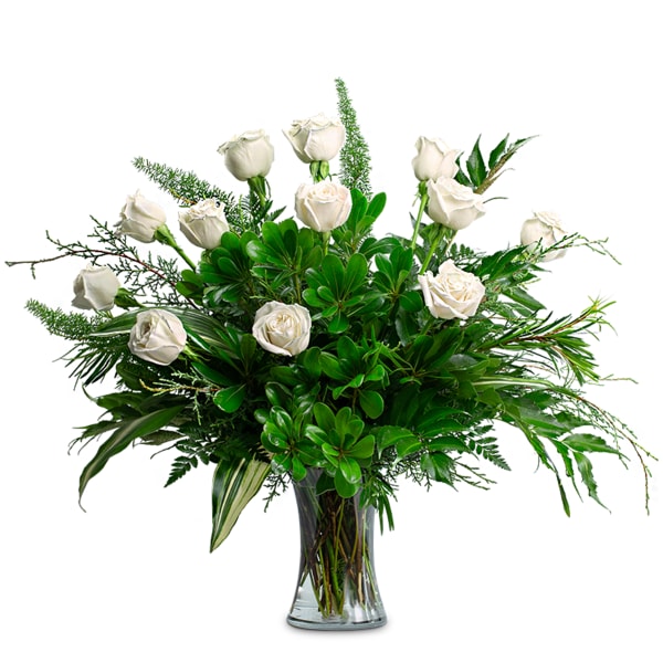 White roses arranged in a clear glass vase with lush greenery