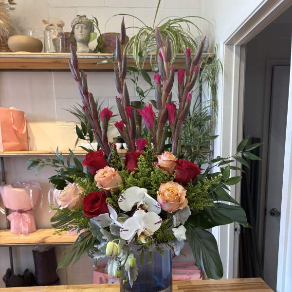Tall bouquet of red and peach roses with white orchids in a blue vase