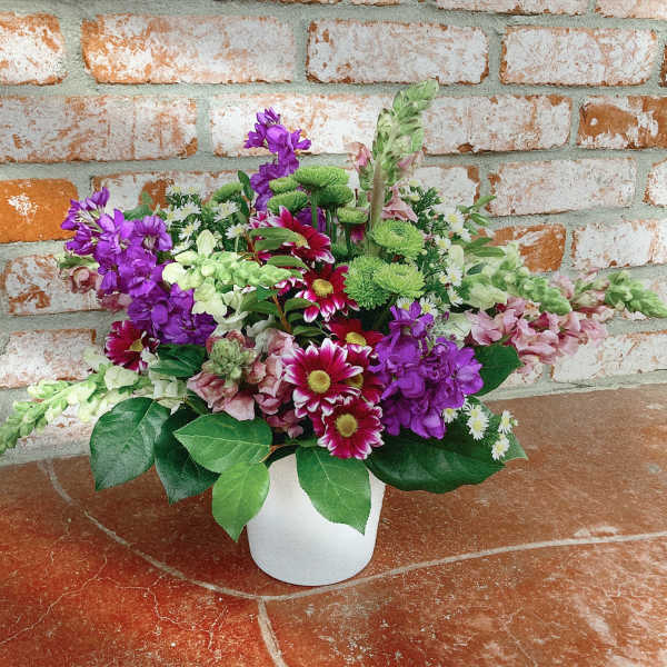 Mixed bouquet of purple, pink, white, and green flowers in a white vase