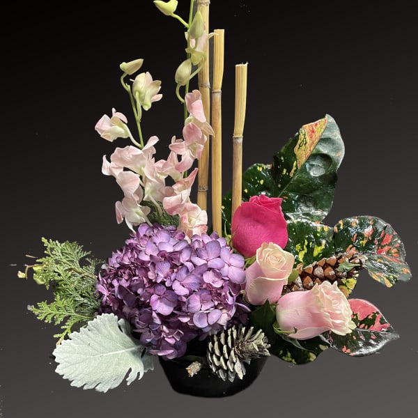Pink roses and purple hydrangea in a black vase with bamboo and pinecones