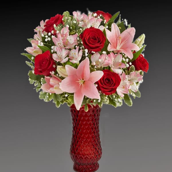 Bouquet of red roses and pink lilies in a red glass vase