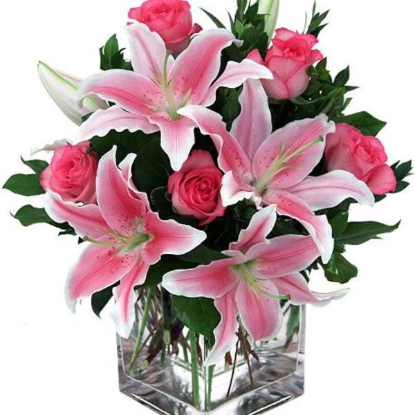 Pink lilies and roses arranged in a clear square vase