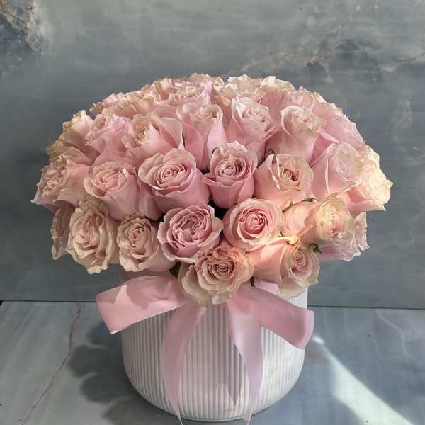 Pink roses arranged in a white ribbed vase with a pink ribbon