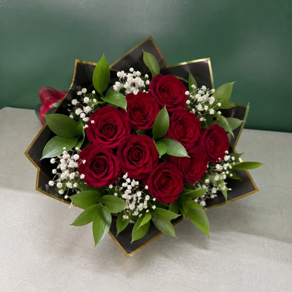 Bouquet of red roses with white baby's breath and green leaves wrapped in black paper