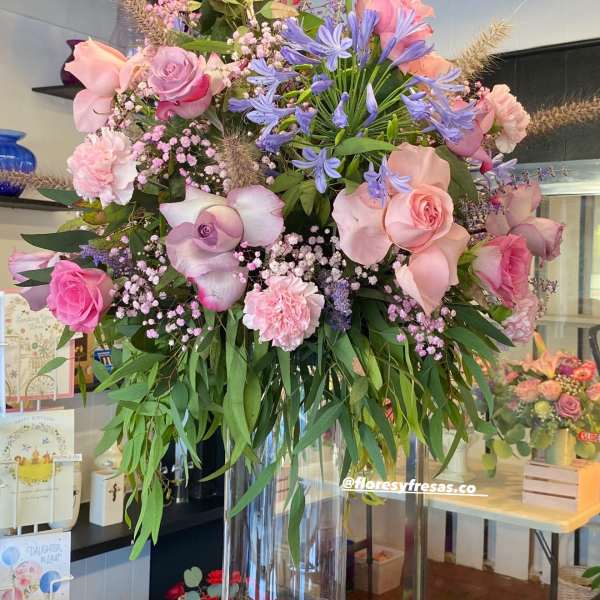 Tall bouquet of pink roses, lavender flowers, and blue blooms in a clear glass vase.
