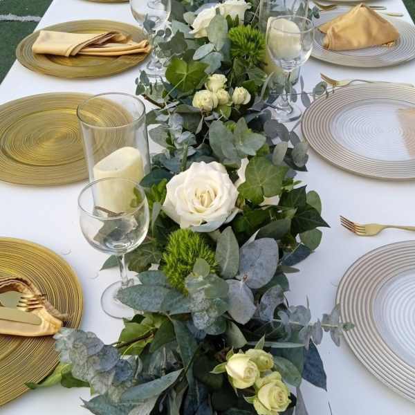 Long table centerpiece with white roses and greenery on a set dining table
