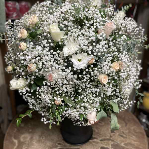 Large white floral arrangement with small pink roses in a black vase