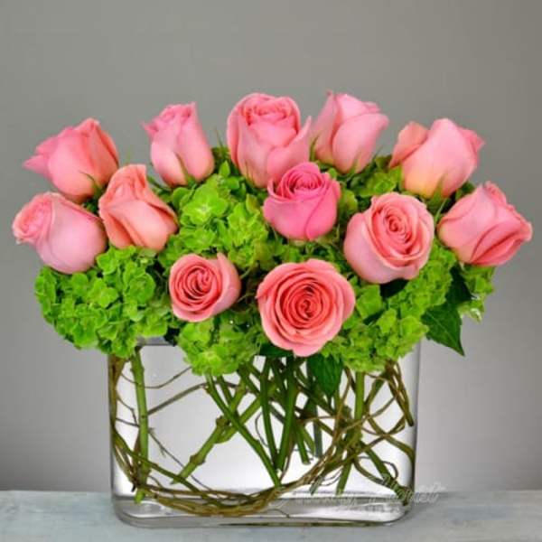 Pink roses arranged with green hydrangeas in a clear glass vase