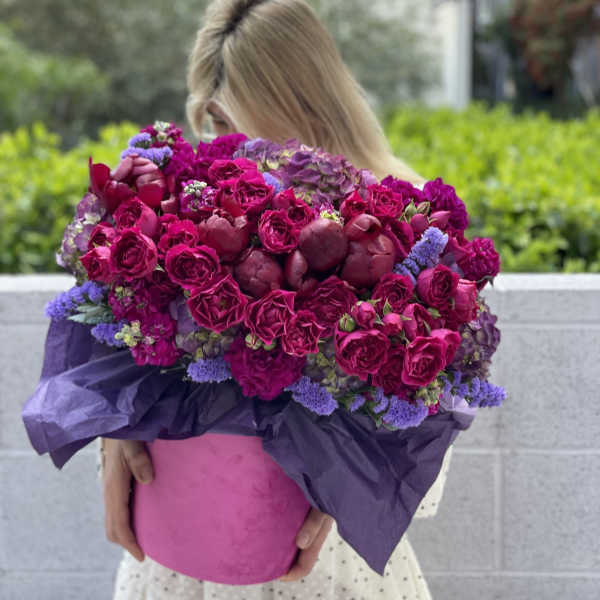 Woman holding a large bouquet of magenta and purple flowers in a pink box