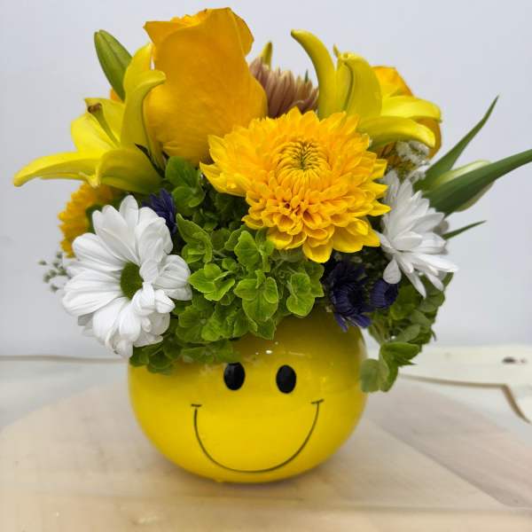Yellow smiley-face container holding a mixed bouquet of yellow, white, and purple flowers