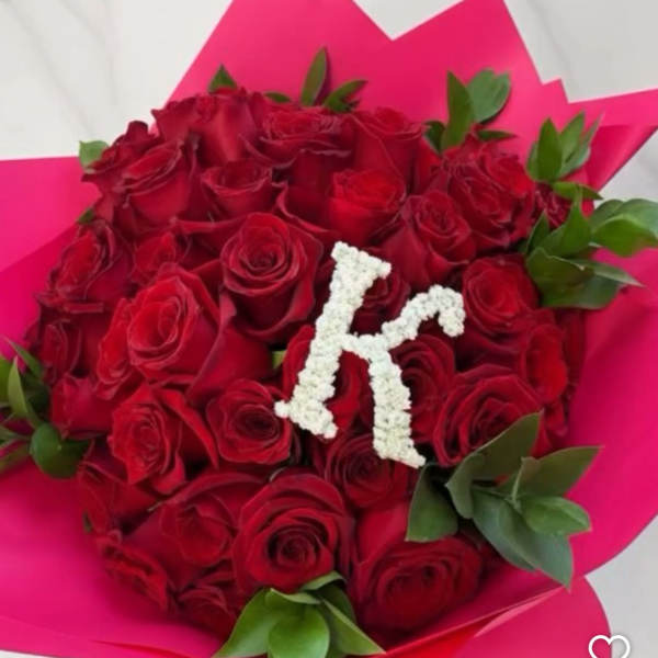 Bouquet of red roses wrapped in bright pink paper with a white floral letter