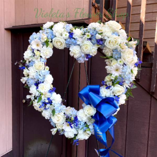 Heart-shaped floral wreath with white and blue flowers and a blue ribbon bow