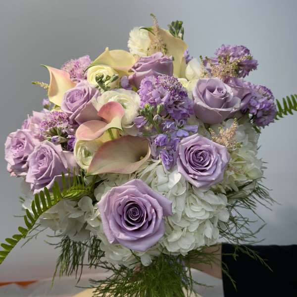 Lavender roses and calla lilies arranged with white hydrangeas.