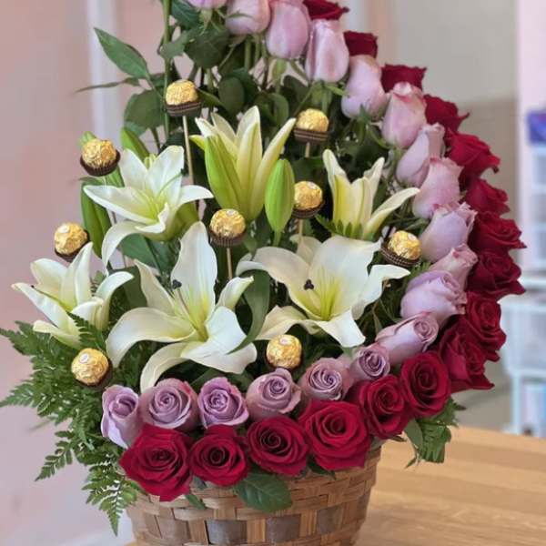Basket arrangement of red and lavender roses with white lilies and gold chocolates