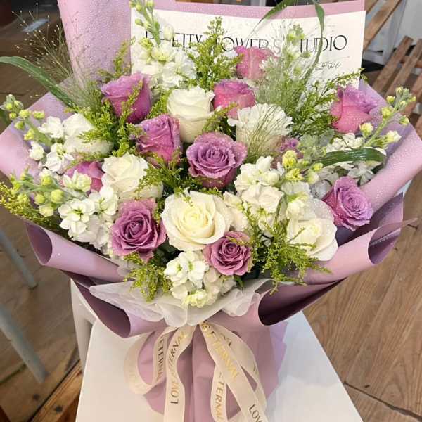 Bouquet of white and lavender roses wrapped in purple paper