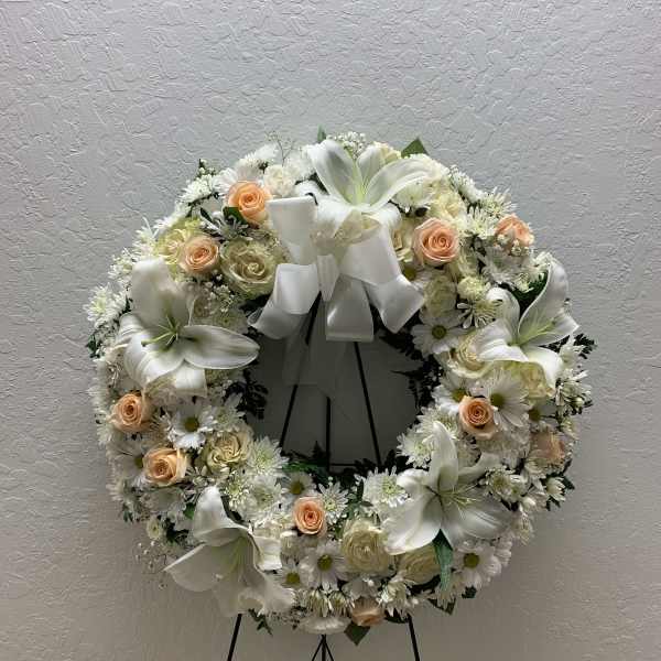 White floral wreath with peach roses and lilies on a stand