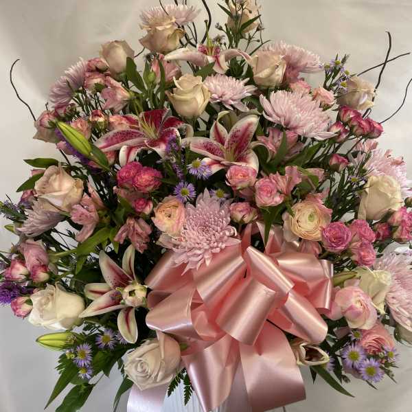 Large pink and white floral arrangement with a satin bow in a white vase