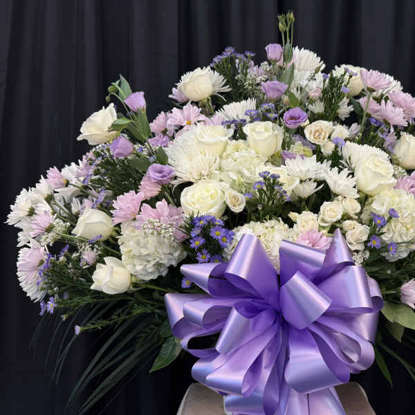 Large lavender and white floral arrangement with a purple ribbon bow
