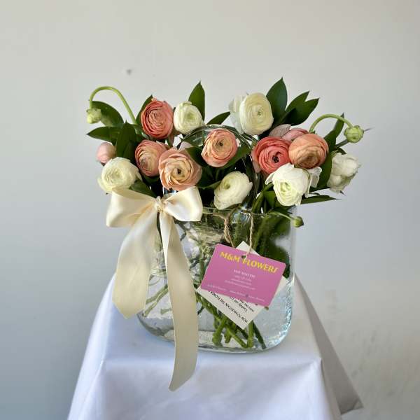 Bouquet of pink and white ranunculus in a glass vase with a ribbon