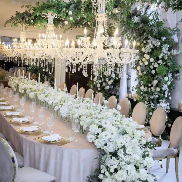 White floral wedding table with chandeliers and a long centerpiece