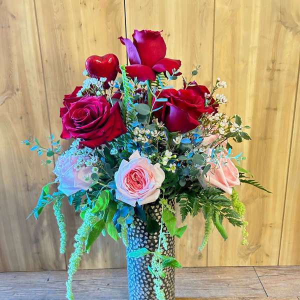 Bouquet of red and pink roses in a tall patterned vase with a heart accent