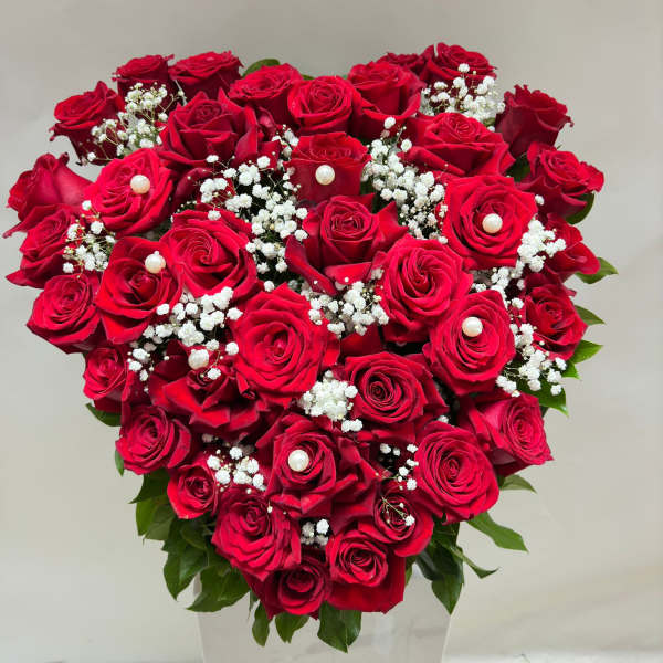 Heart-shaped bouquet of red roses with baby's breath in a white vase