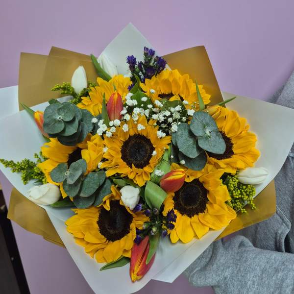 Bouquet of sunflowers, tulips, and white filler flowers wrapped in paper