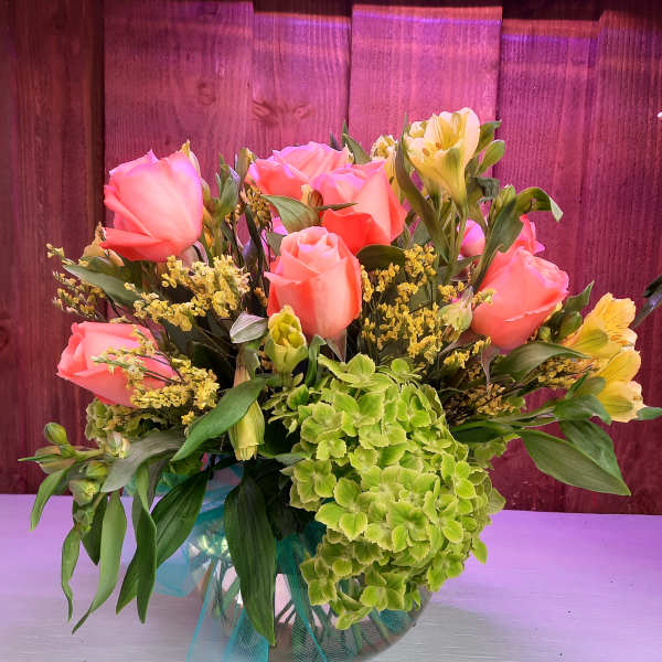 Pink roses and green hydrangea in a glass vase with yellow filler flowers