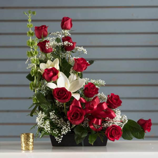 Asymmetrical arrangement of red roses and white lilies in a black container with a red ribbon bow.