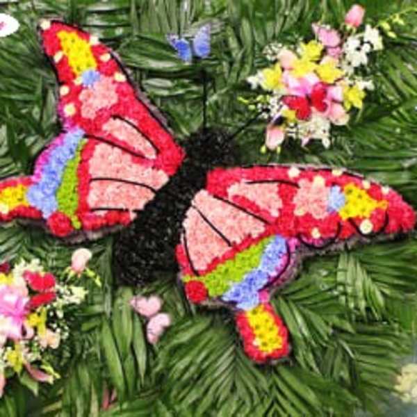 Butterfly-shaped floral tribute with colorful flower clusters on a green foliage background