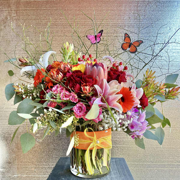 Colorful mixed flower arrangement in a glass vase with butterfly picks