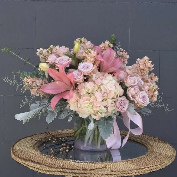 Pink and blush floral arrangement in a glass vase with a ribbon