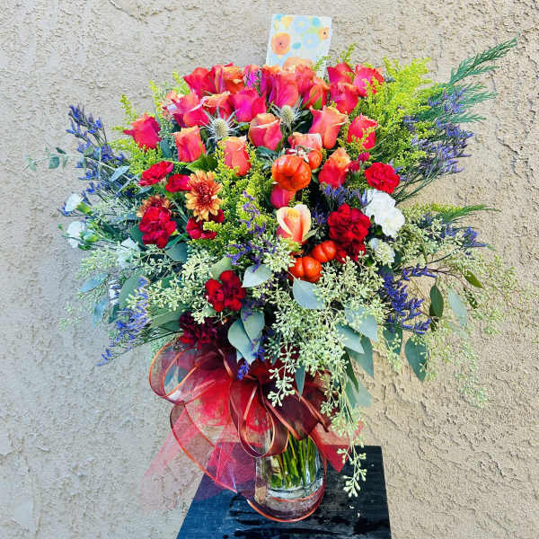 Large bouquet of pink roses and mixed flowers in a glass vase with a red ribbon