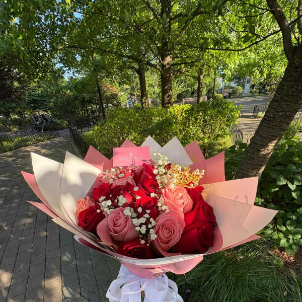 Handheld bouquet of red and pink roses with baby's breath in pink wrapping