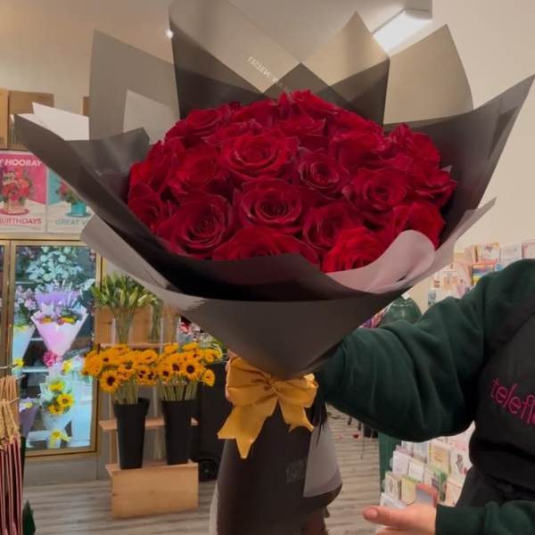 Bouquet of red roses wrapped in black paper with a gold ribbon