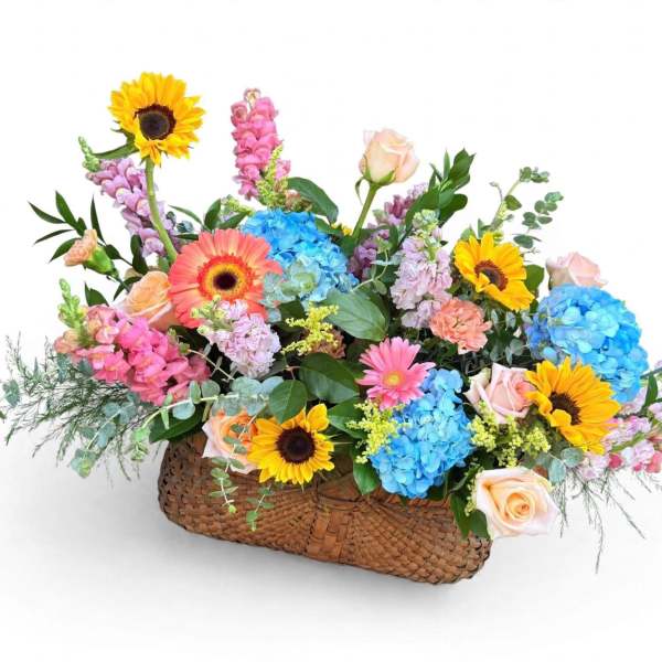 Mixed bouquet in a woven basket with sunflowers, roses, and blue hydrangeas