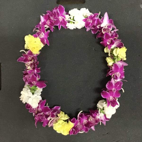 Purple and white orchid lei with yellow accents on a black surface