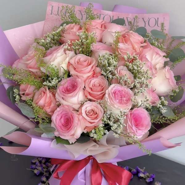 Pink rose bouquet wrapped in lavender paper with a red ribbon