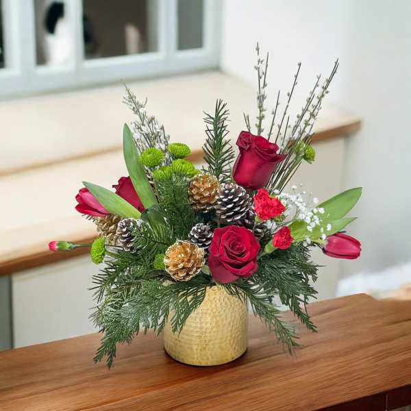 Red roses and tulips arranged in a gold vase with pinecones