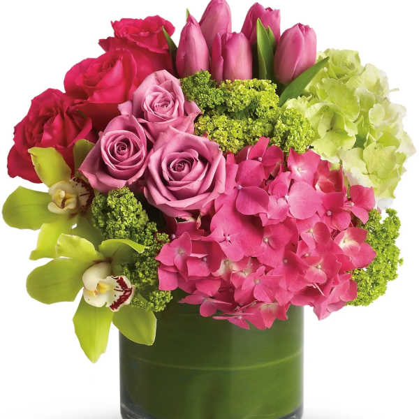 Compact arrangement of pink roses, tulips, and hydrangeas with green orchids in a leaf-lined glass cylinder vase