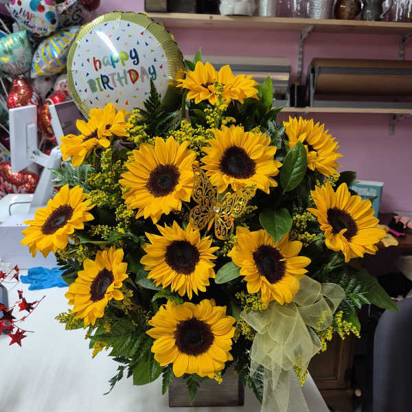 Sunflower arrangement with a birthday balloon and ribbon in a wooden container.