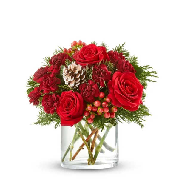 Red roses and carnations in a clear glass vase with pinecones and berries