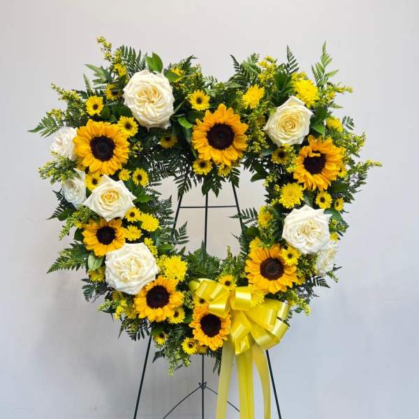 Heart-shaped floral wreath with sunflowers and white roses on a stand