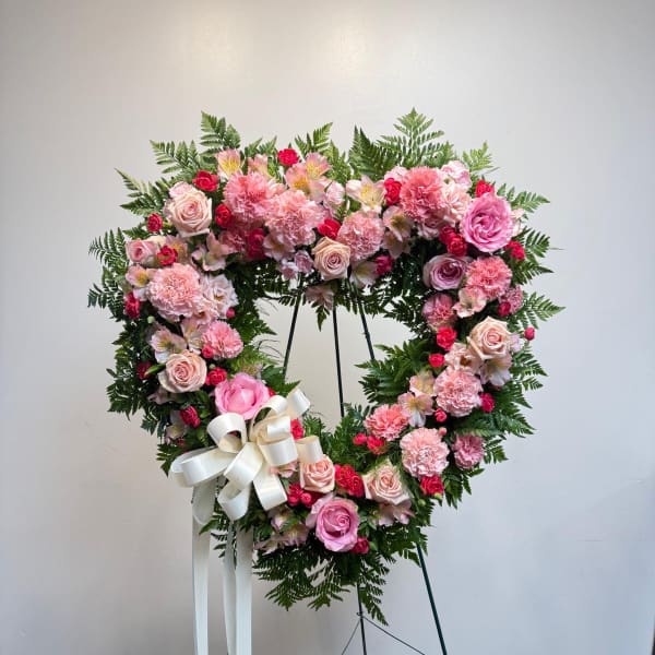 Heart-shaped pink floral wreath on a stand with a white ribbon bow