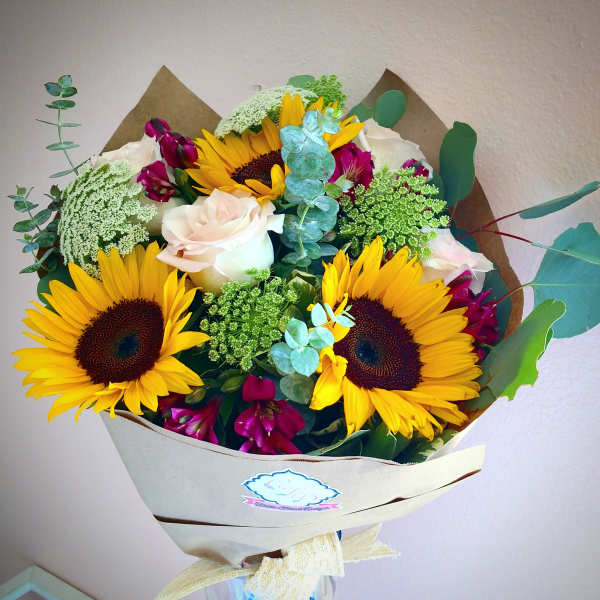 Bouquet of sunflowers, white roses, and magenta flowers wrapped in paper