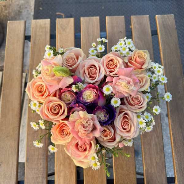 Round bouquet of blush and peach roses with small white daisies
