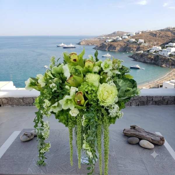 Green and white floral arrangement in a clear glass vase with trailing stems